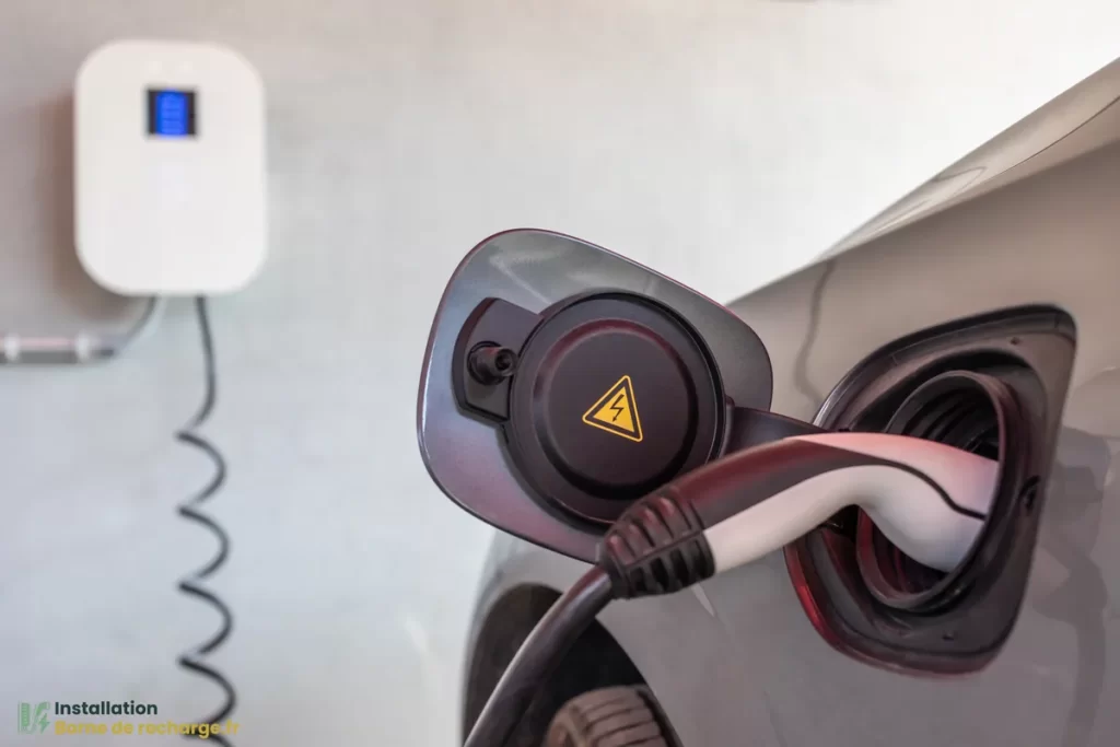 Une prise de recharge branchee sur une voiture, avec la borne visible en arriere-plan.